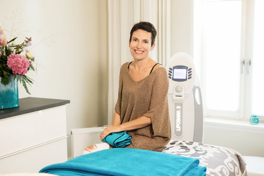 Heilpraktikerin Nadine Herz sitzt in ihrer Praxis in Potsdam auf einer Behandlungsliege, im Hintergrund steht das Liposaner-Gerät zur Körperformung und Gewichtsreduktion.